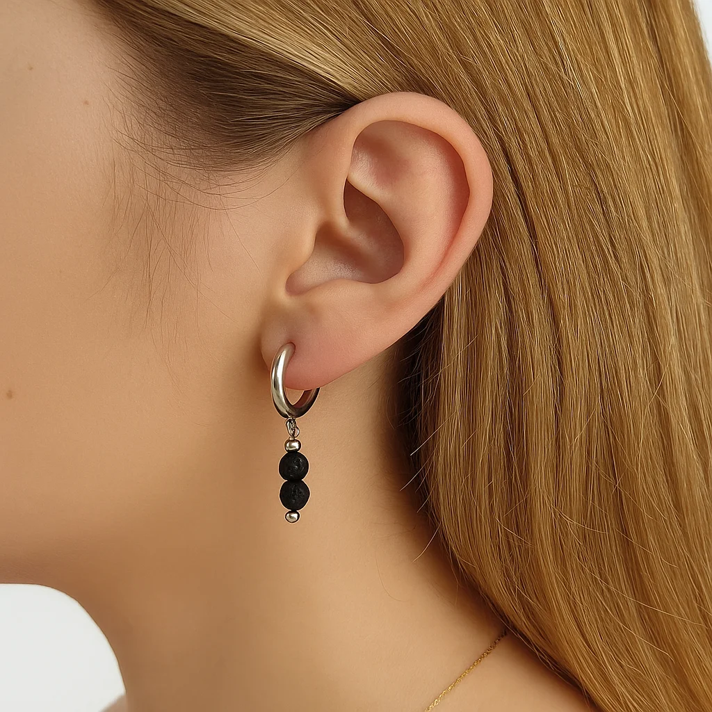 pendientes de aro gruesos y plateados, con un colgante formado por dos cuentas de piedra volcánica negra de textura porosa.