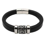 Primer plano de un brazalete masculino con una correa de cuero negro redonda y un adorno central de acero con un diseño orgánico calado, sobre fondo blanco.