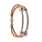 Una pulsera de cuero marrón claro con una pieza central de acero formada por dos barras curvas y esferas, y un cierre magnético plateado.