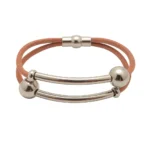 "Primer plano de Pulsera Doble con Tubos de Acero y bolas de metal, sobre bandas de cuero negro."