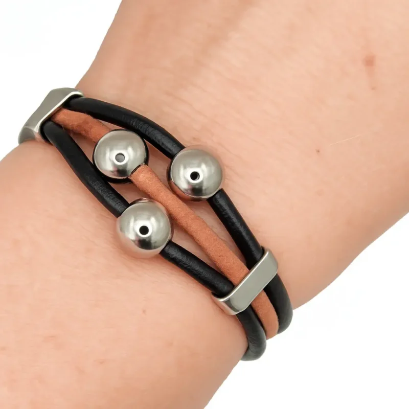 Una pulsera de hombre con tres tiras de cuero, dos negras y una marrón, adornada con tres esferas de acero en el centro y un cierre de seguridad.