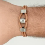 Brazalete de cuero con detalles de metal plateado y diseño geométrico de aros.