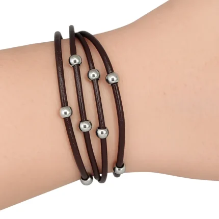Una pulsera de varias tiras de cuero negro sujeta por nudos y pequeñas cuentas doradas distribuidas a lo largo de las tiras.