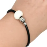 Pulsera de cuero fino con abalorios geométricos (cuadrado y esferas) y gancho de metal.
