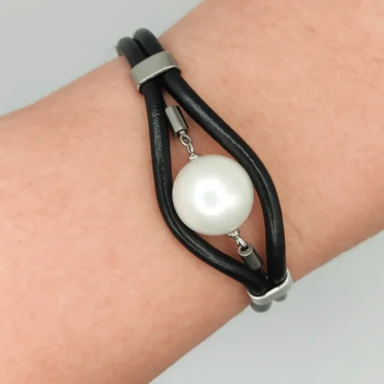 "Primer plano de pulsera con bandas de cuero negro y beige, y gran cuenta central negra con terminales de acero."