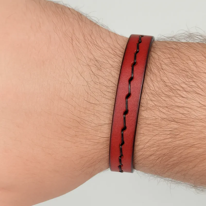 Pulsera de cuero plano de color marrón rojizo o caoba, con un pespunte grueso de hilo negro en los bordes y un cierre magnético de metal plateado.