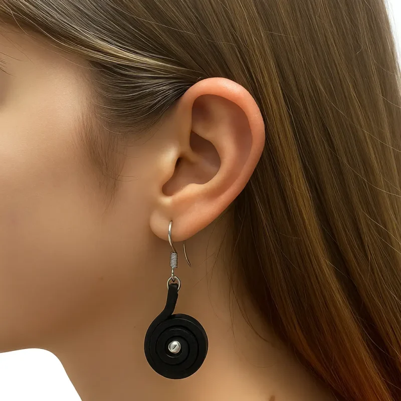 Pendiente artesanal con cuero en caracol en capas y detalle metálico central, colgado de un gancho plateado.